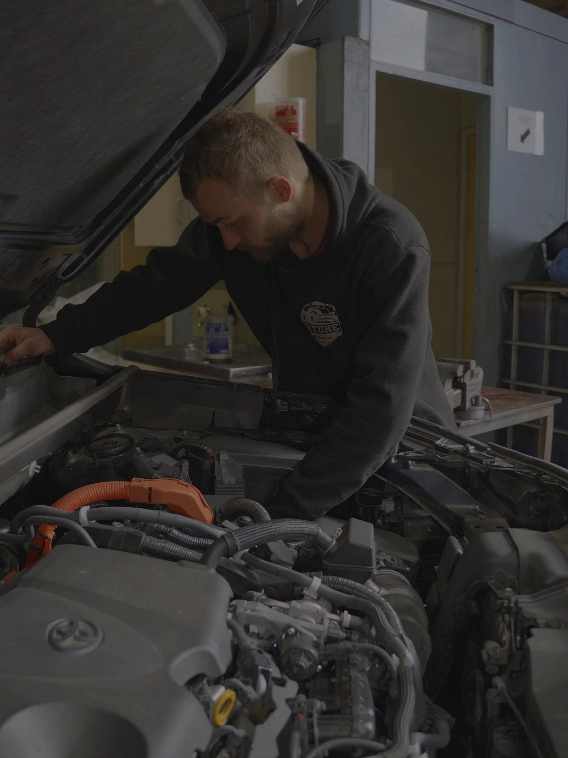 Mechanic inspecting a car engine with the hood open in a workshop