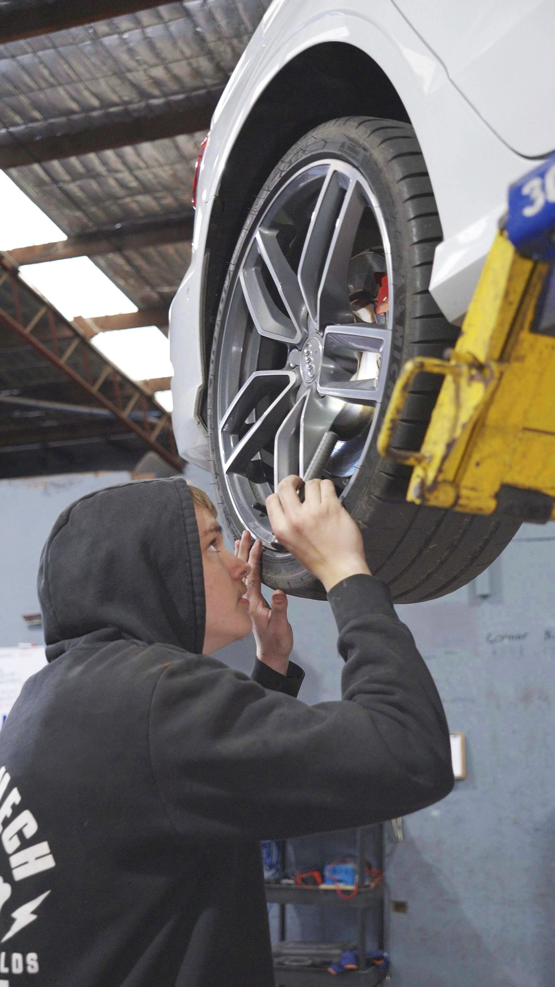 Mechanic inspecting a car wheel on a lift in an auto shop