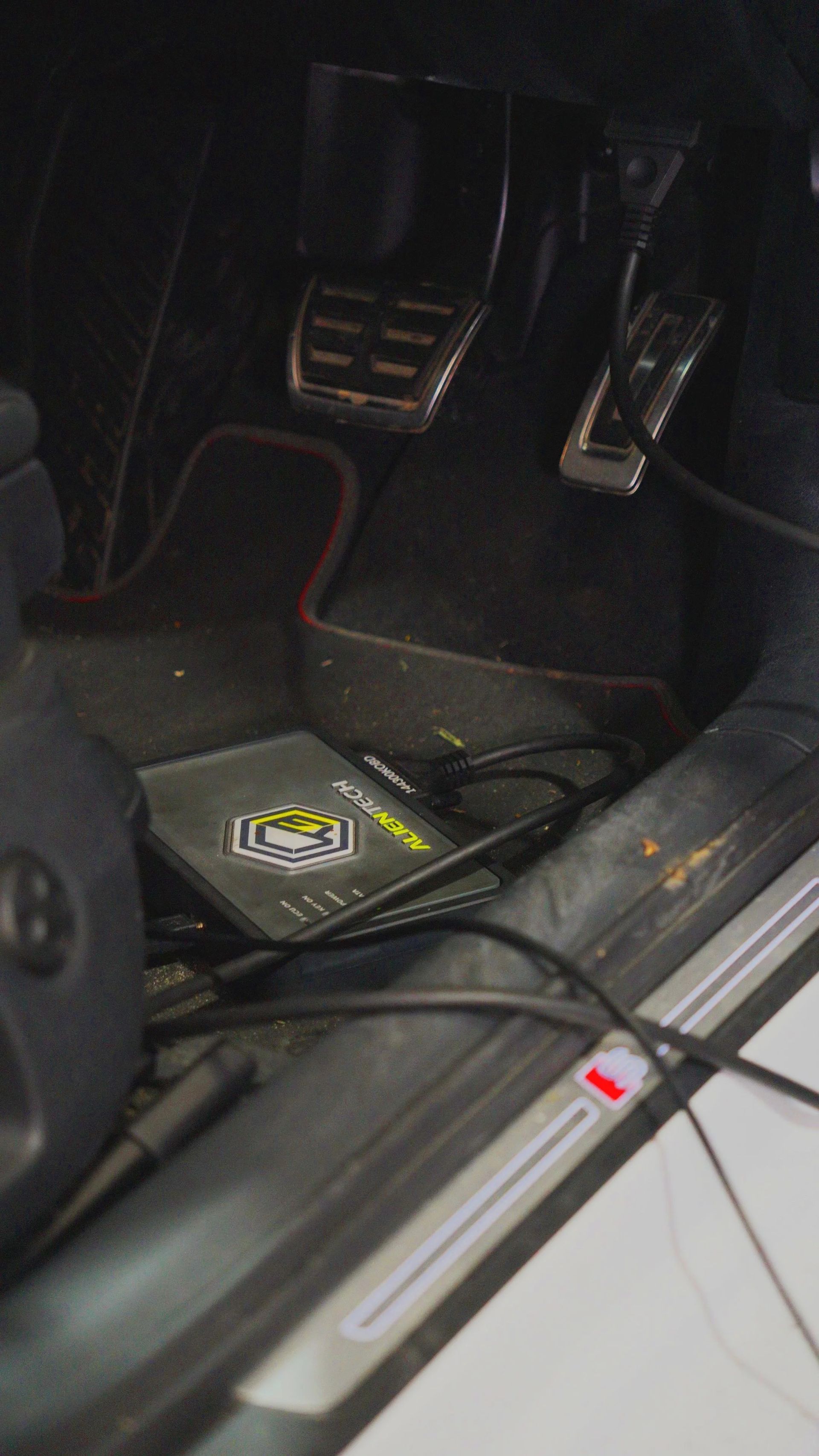 Car engine with hood open in an auto repair shop, showing the engine bay and workshop tools.