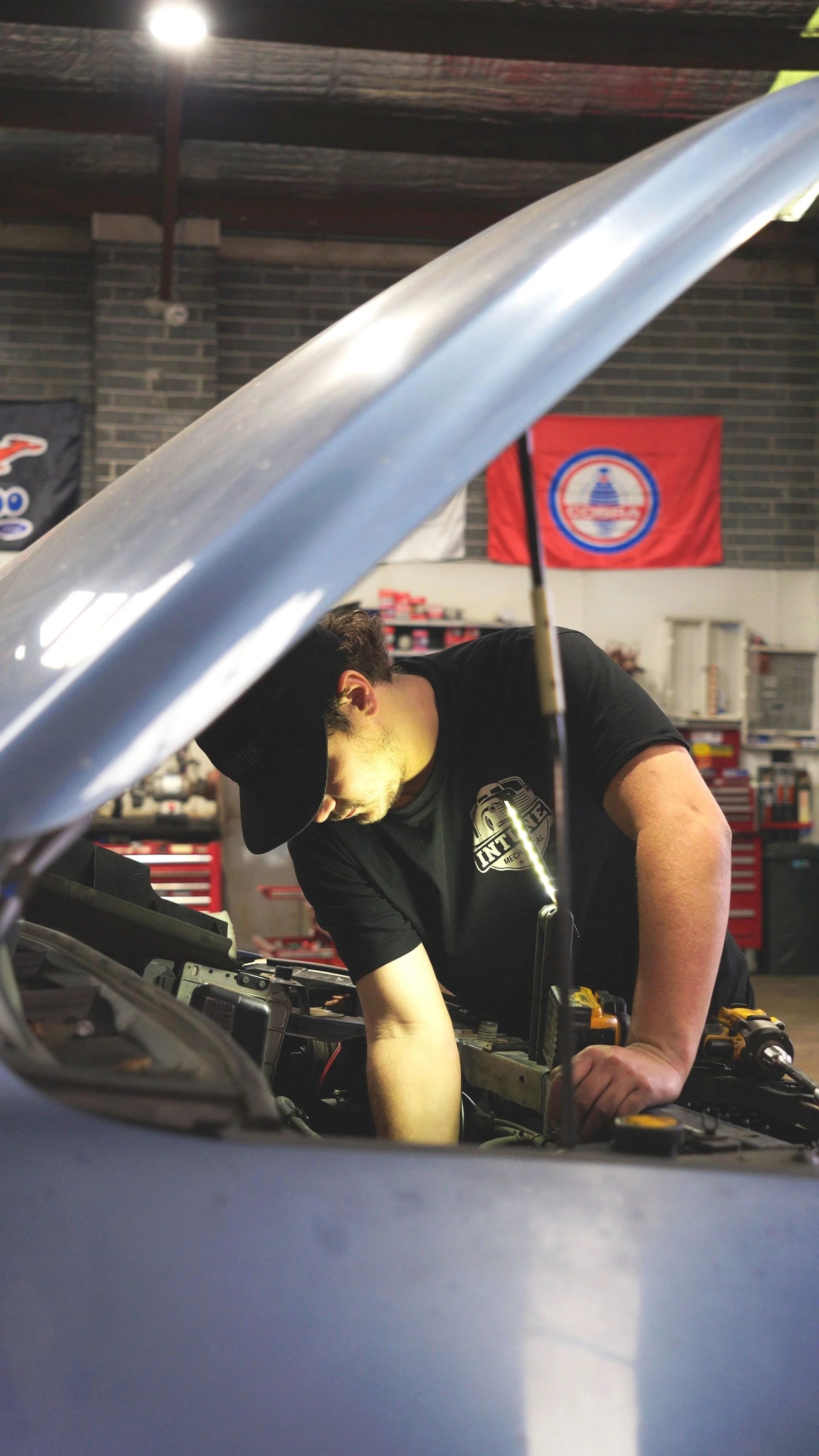 Mechanic working under a raised car hood in an auto shop