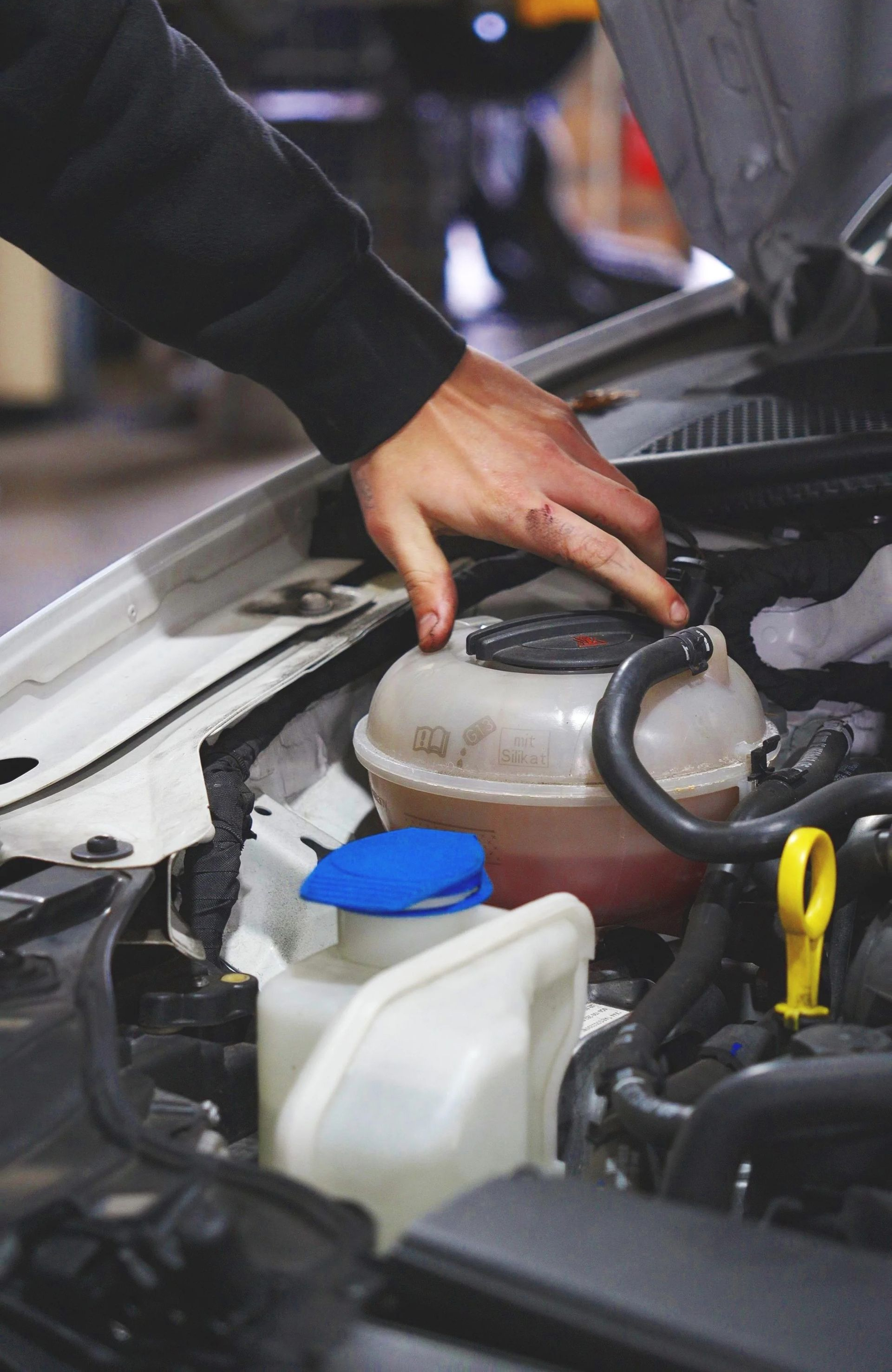 Hand checking a car engine coolant reservoir under the hood.