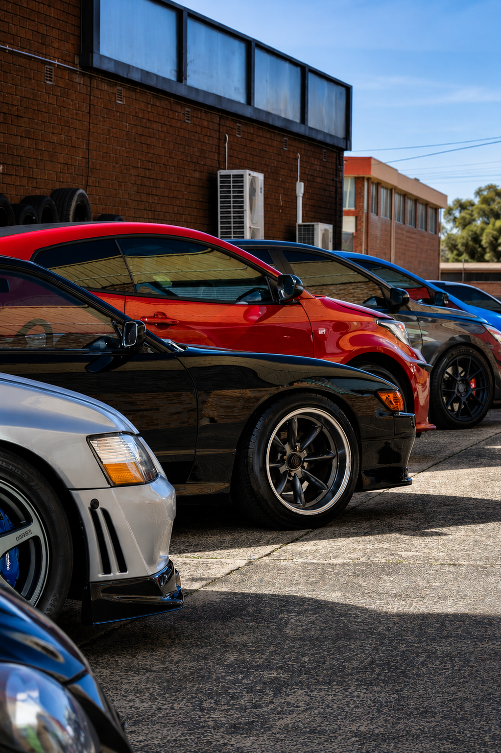 Parked sports cars in a lot beside a brick building on a sunny day