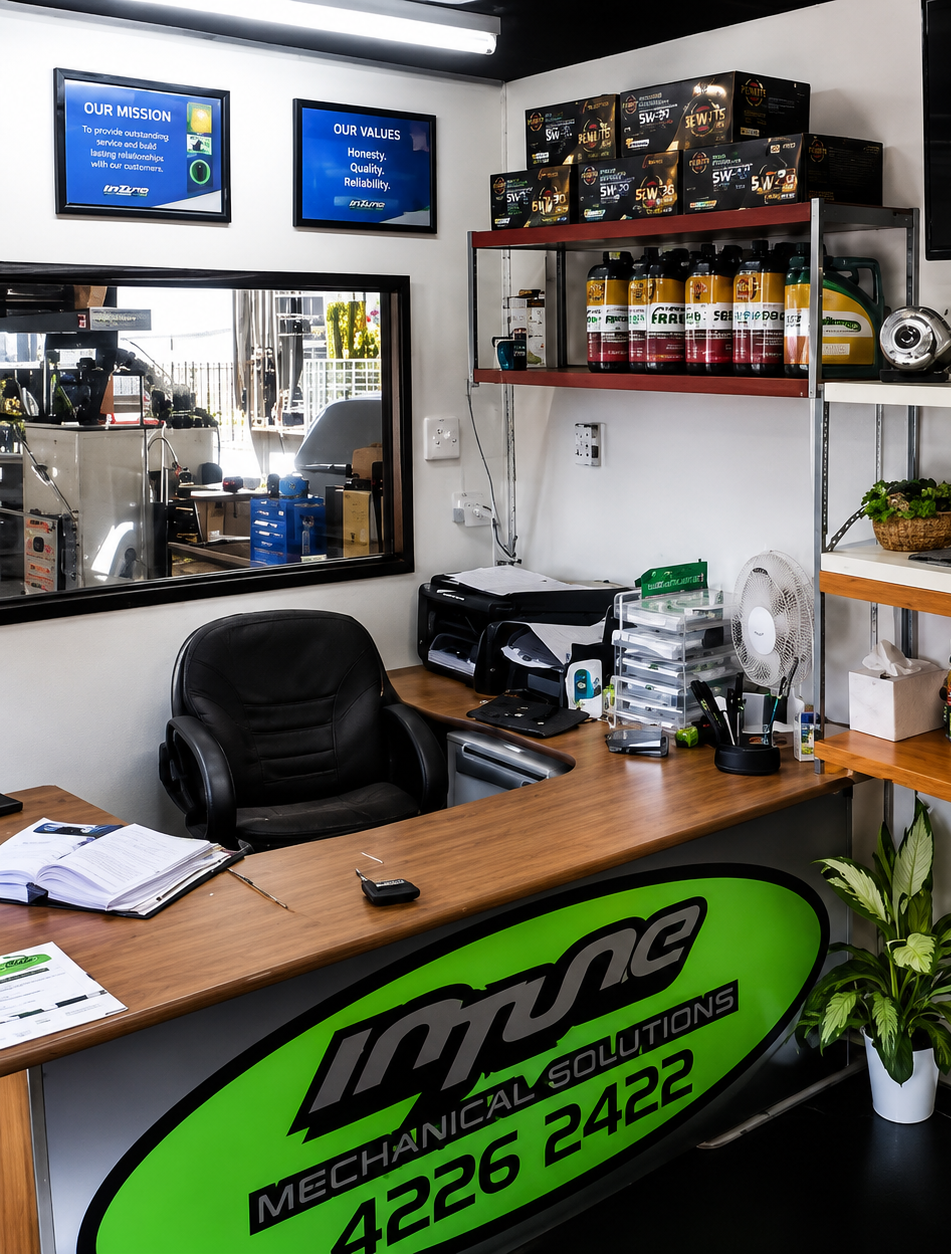 Auto mechanic shop office with wooden desk, black chair, shelves of products, and green counter sign.