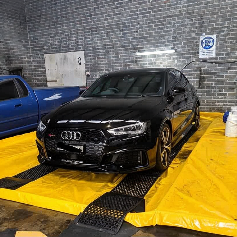 Black Audi SUV on a yellow car lift in a brick-walled auto shop