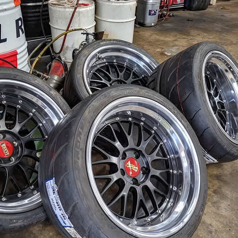 Four black-and-chrome alloy wheels with tires stacked in a garage or workshop.