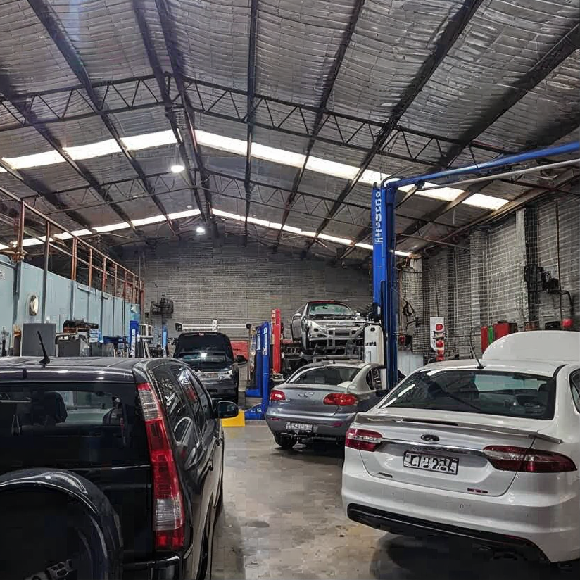 Black Audi sedan parked indoors on a bright yellow floor beside a blue car in a brick-walled garage