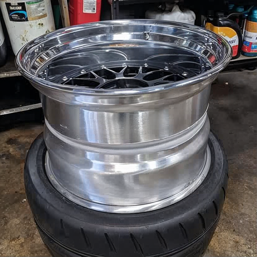 Chrome car wheel rim resting on a black tire in a garage workshop.