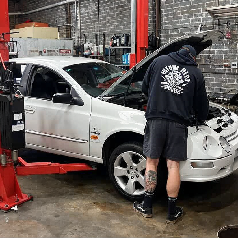 Mechanic inspecting a white car with its hood open in an auto repair shop
