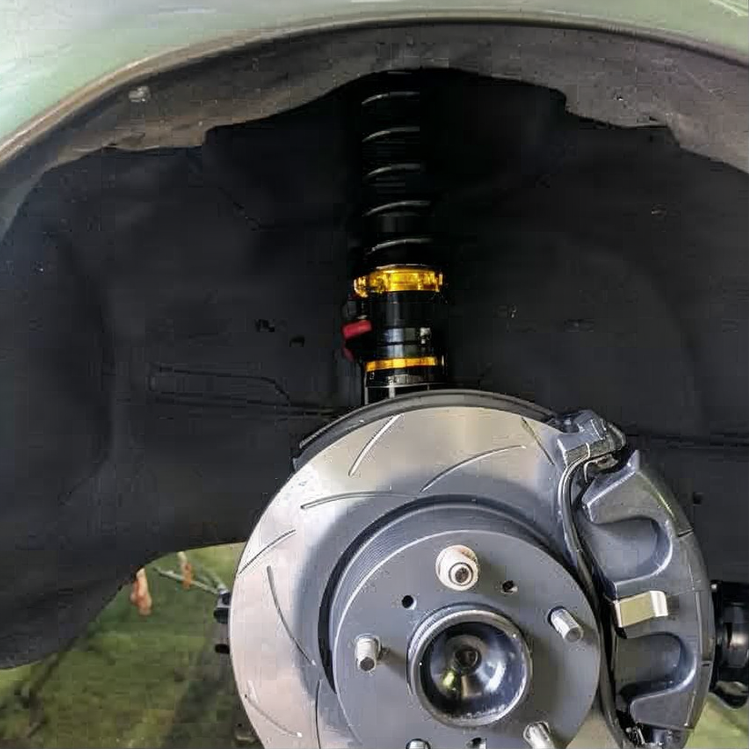 Car wheel well showing brake rotor, caliper, and coilover suspension assembly