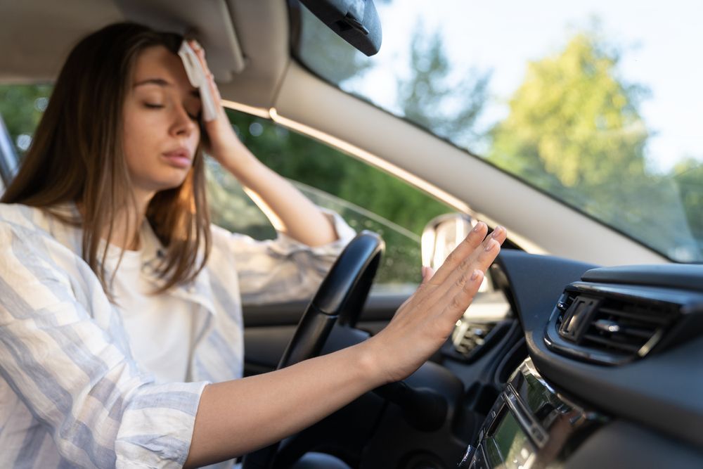 Woman sitting in a car, holding her head and reaching toward the steering wheel, looking stressed