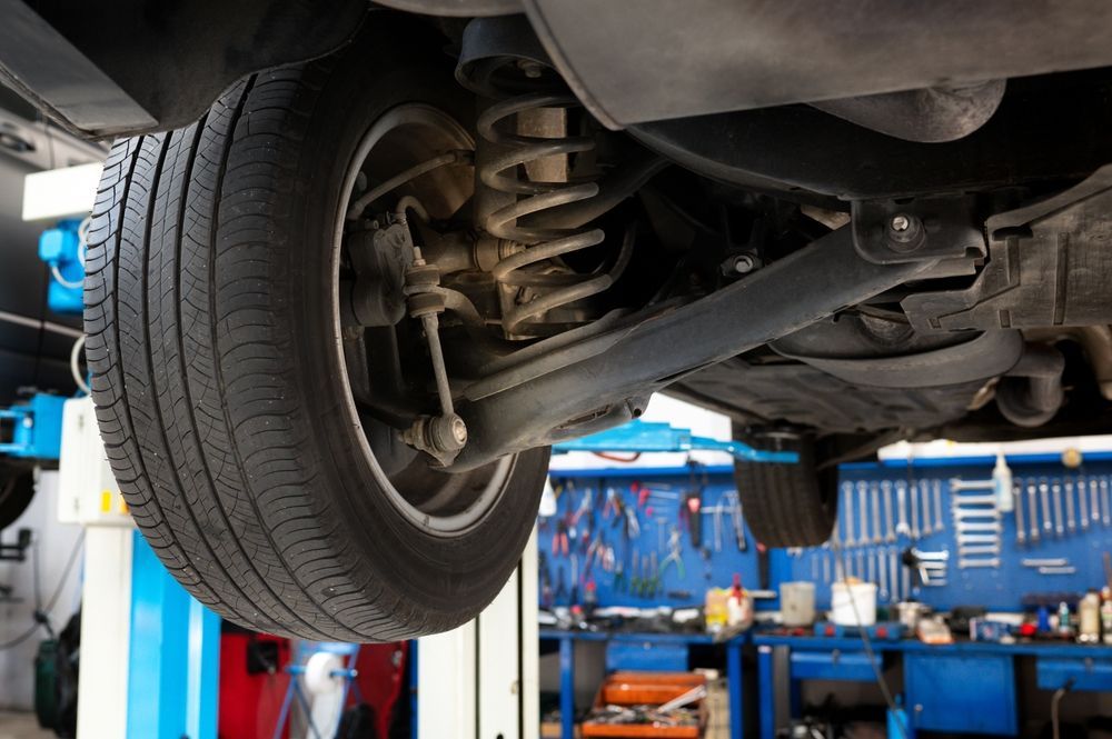 Undercarriage of a car on a lift in an auto repair shop with tools and equipment in the background