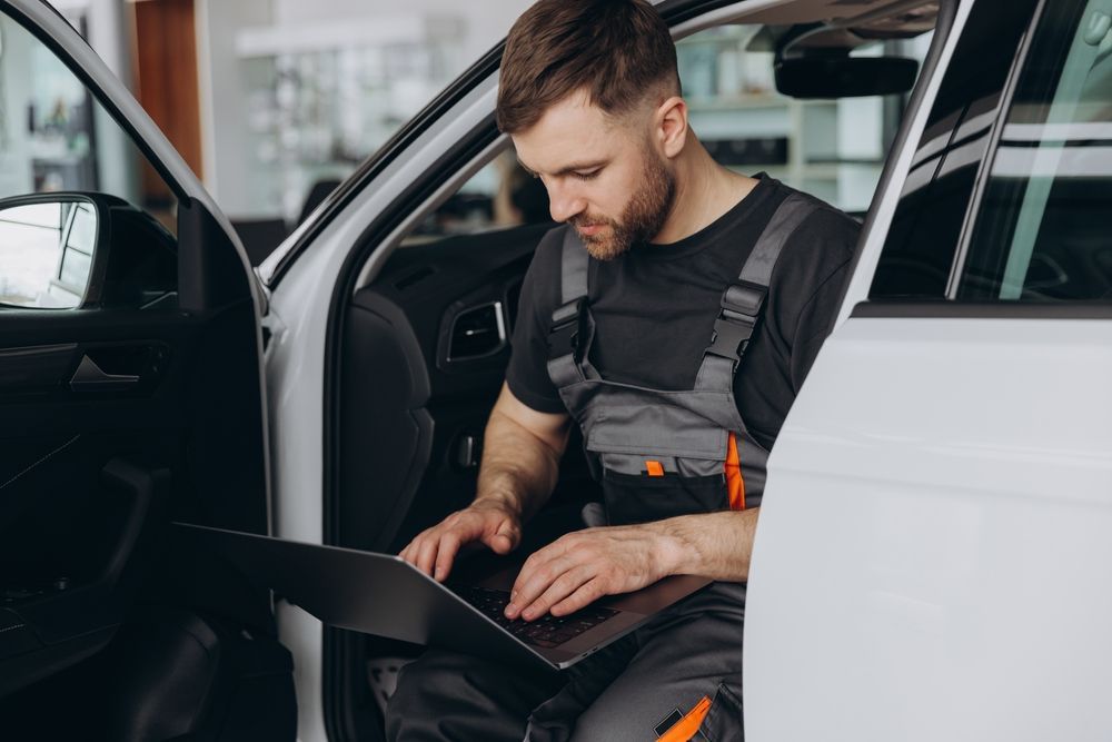 Mechanic using a laptop while seated in an open car door