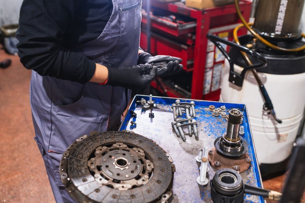 Mechanic in gloves working beside a brake rotor and disassembled car parts on a shop cart