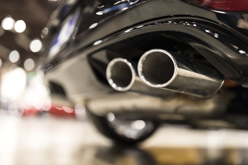 Close-up of dual chrome car exhaust pipes on a black vehicle, with blurred lights in the background