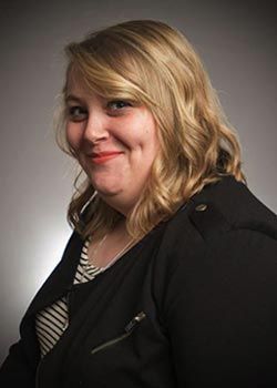 A woman in a black jacket and striped shirt is smiling for the camera.