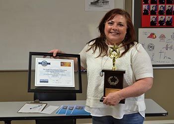 A woman is holding a trophy and a certificate in front of a table.