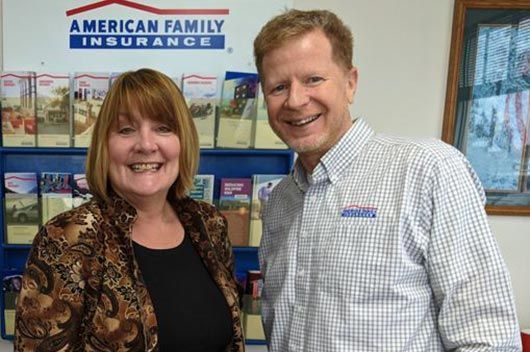 A man and a woman are smiling in front of an american family insurance sign