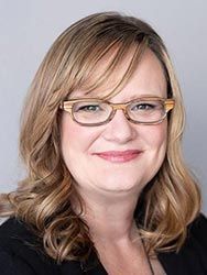 A woman wearing glasses and a black shirt is smiling for the camera.