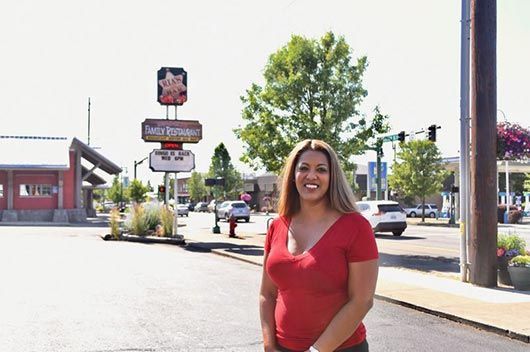 A woman in a red shirt is standing on the sidewalk in front of a sam 's club sign.