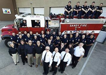 A group of firefighters are posing in front of a sandy fire truck