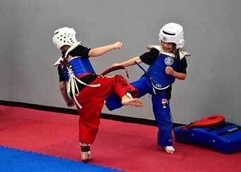 Two young boys are practicing martial arts on a mat in a gym.