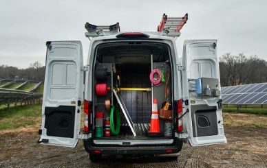 A white van is parked in a field with its doors open.
