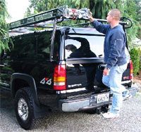 A man is standing next to a truck with a ladder on top of it.