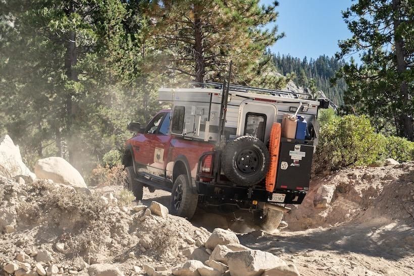 A red truck is driving down a dirt road in the woods.