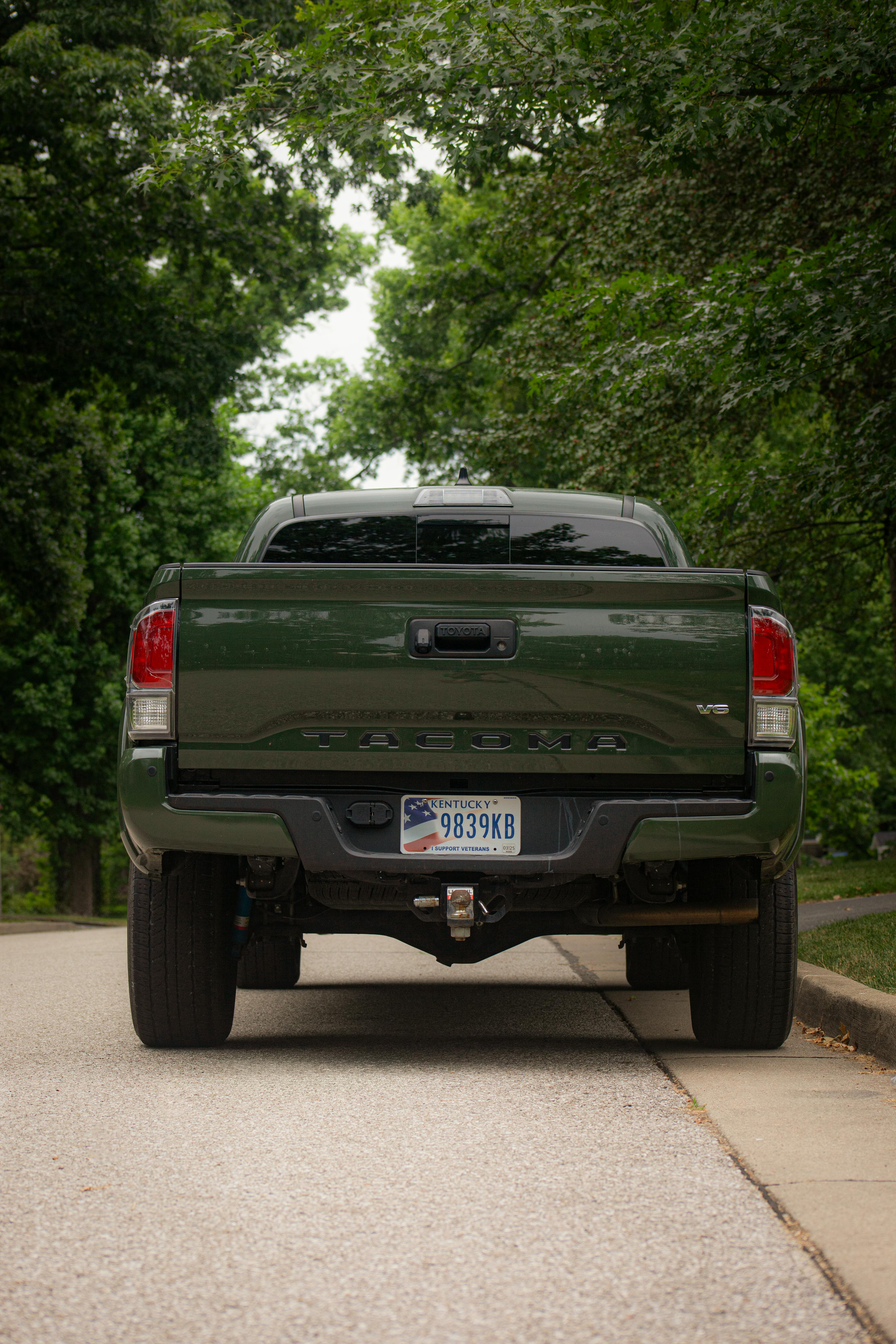 The back of a green truck is parked on the side of the road.