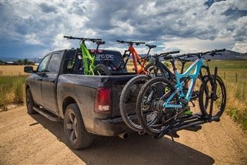 A truck with bikes in the back is parked on a dirt road.