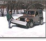 A man is standing next to a jeep with a snow plow on it.