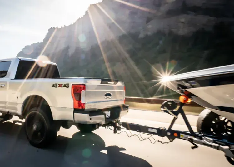 A white truck is towing a boat on a trailer.