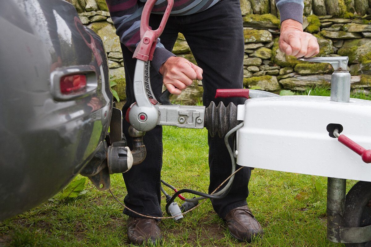 A man is attaching a trailer to a car Littleton Colorado Common Trailer Hitch Safety Issues