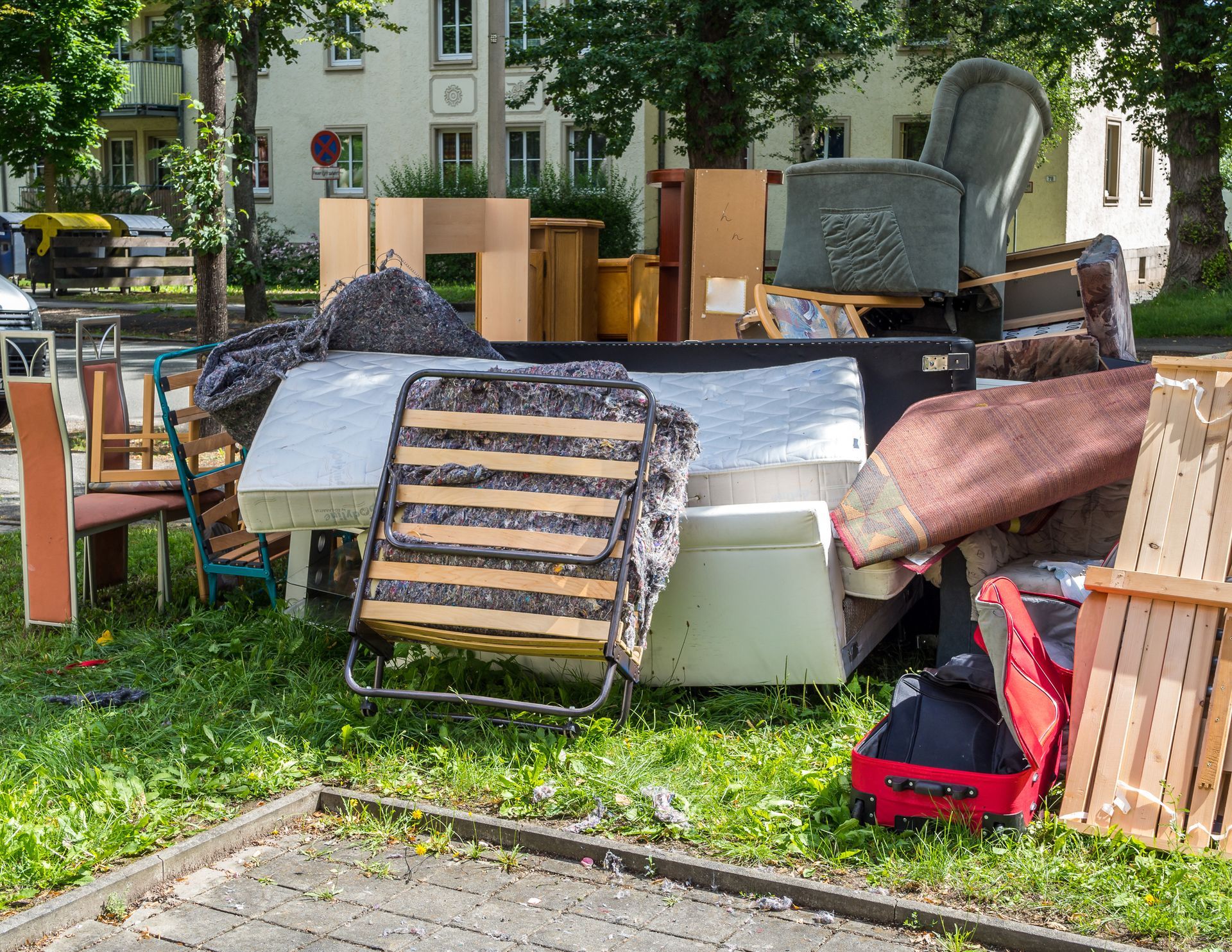 Pile of discarded furniture and household items on a curb, including a mattress, chair, and wooden frames.