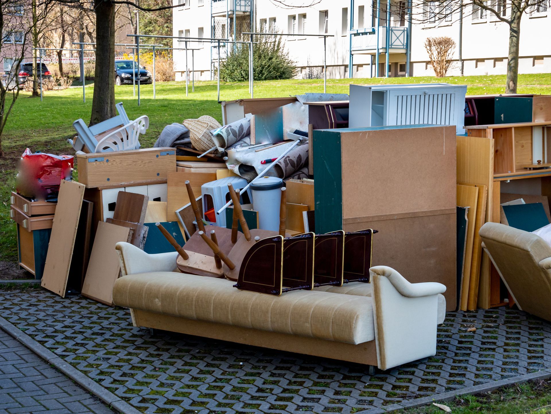 Pile of discarded furniture, including a couch, on a paved area, possibly for disposal in a residential area.