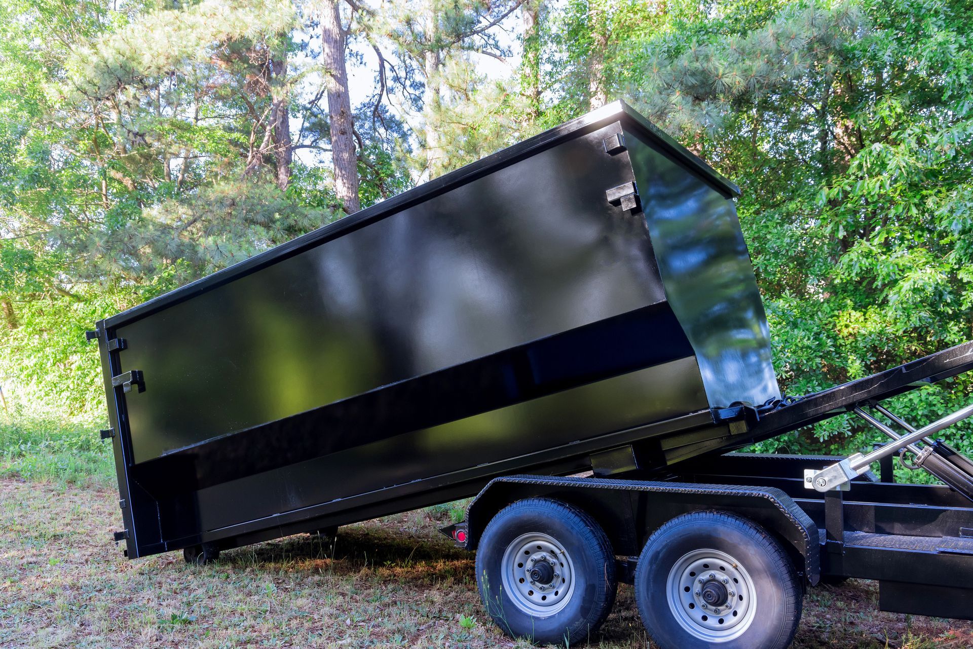 Trailer carrying wooden furniture, covered with a blue tarp, parked on a brick-paved area next to a car.