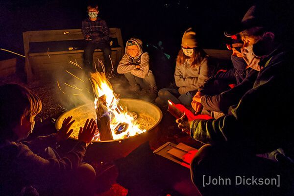 A group of adolescents are sitting around a fire pit at night.