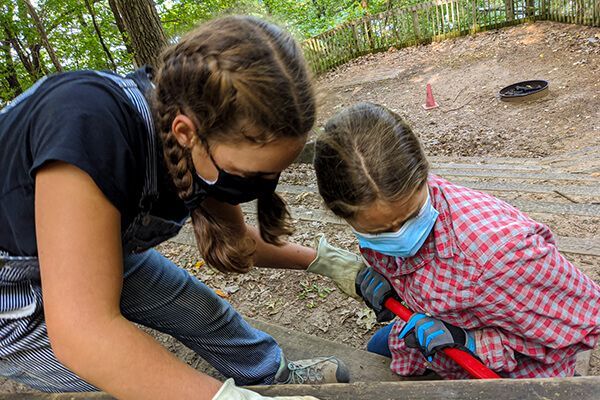 Two adolescents wearing masks are working in the dirt.