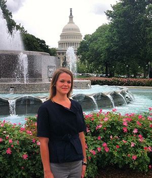 A woman is standing in front of a fountain in front of the capitol building.