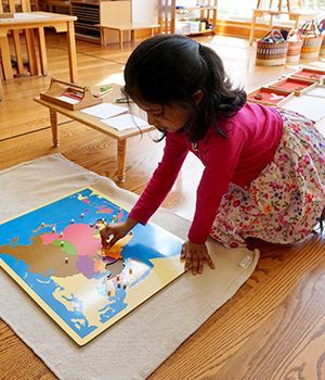 A little girl is kneeling on the floor playing with a map of the world.