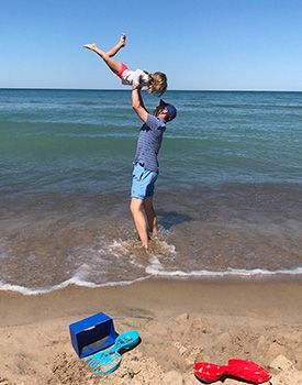 A father plays by tossing his daughter into the air as they stand at the edge of the sea