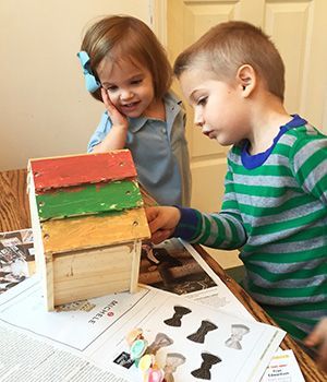 A boy and a girl are playing with a small wooden bird house