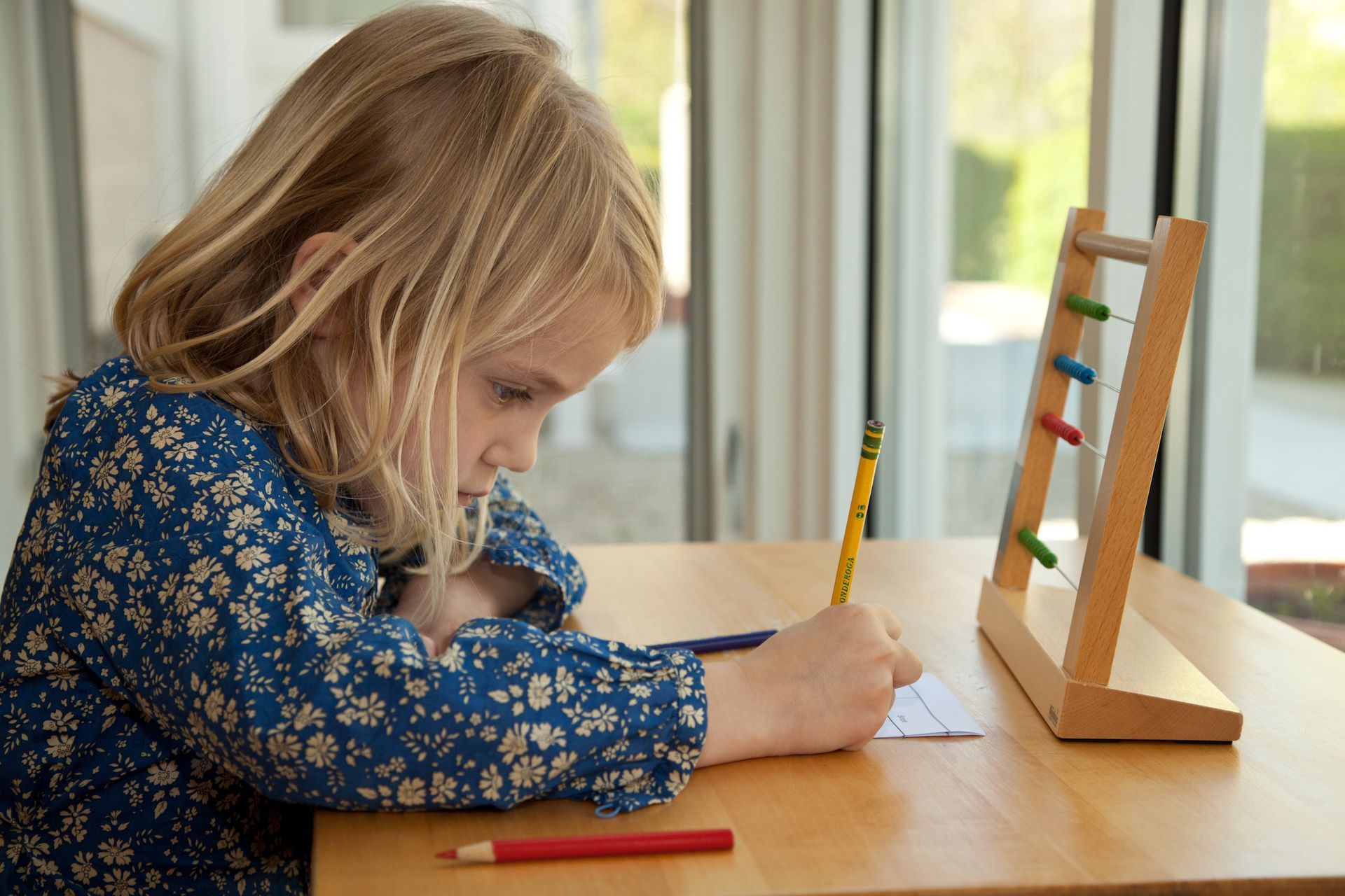 A Montessori child is sitting at a table writing with a pencil.