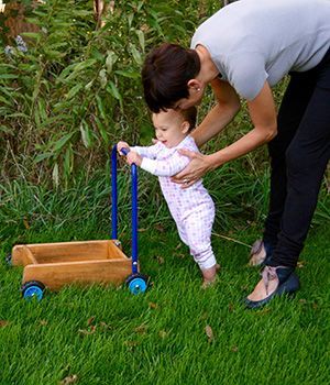 A woman is helping a baby walk with a wooden walker.