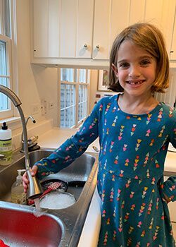 A little girl is washing dishes in a kitchen sink.