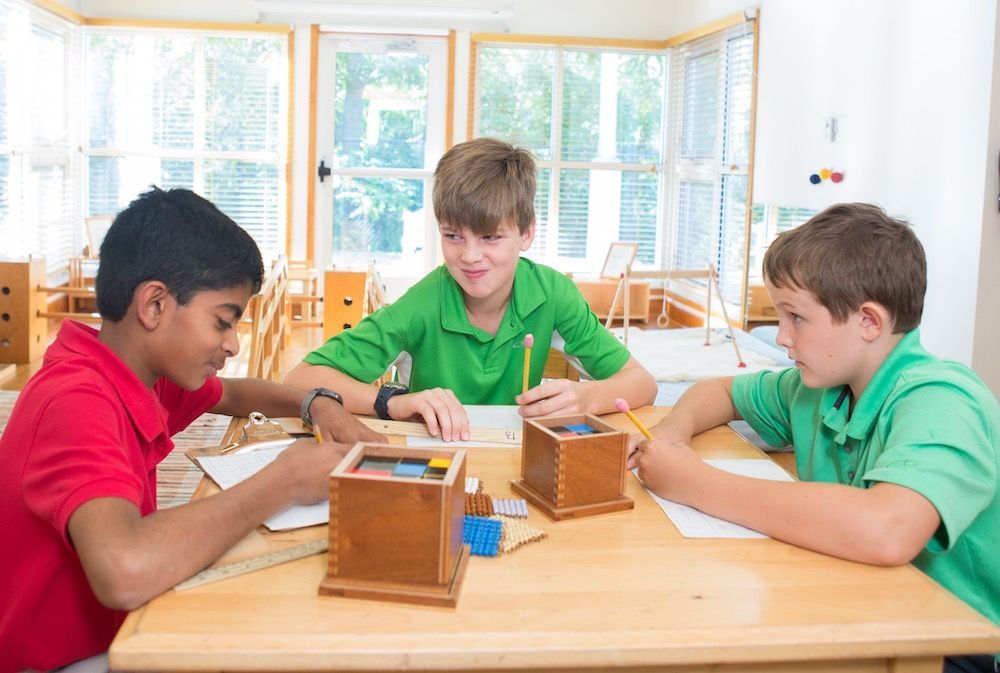 Three Montessori Elementary students socialize while working together on a math material. 