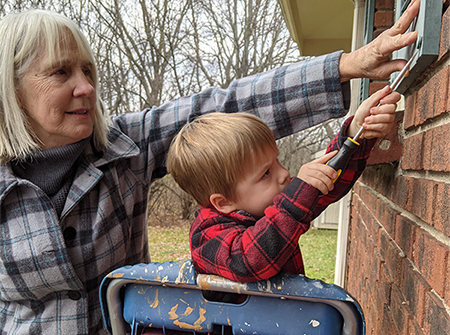 A young child on a ladder uses a screwdriver to make a home repair with adult assistance 