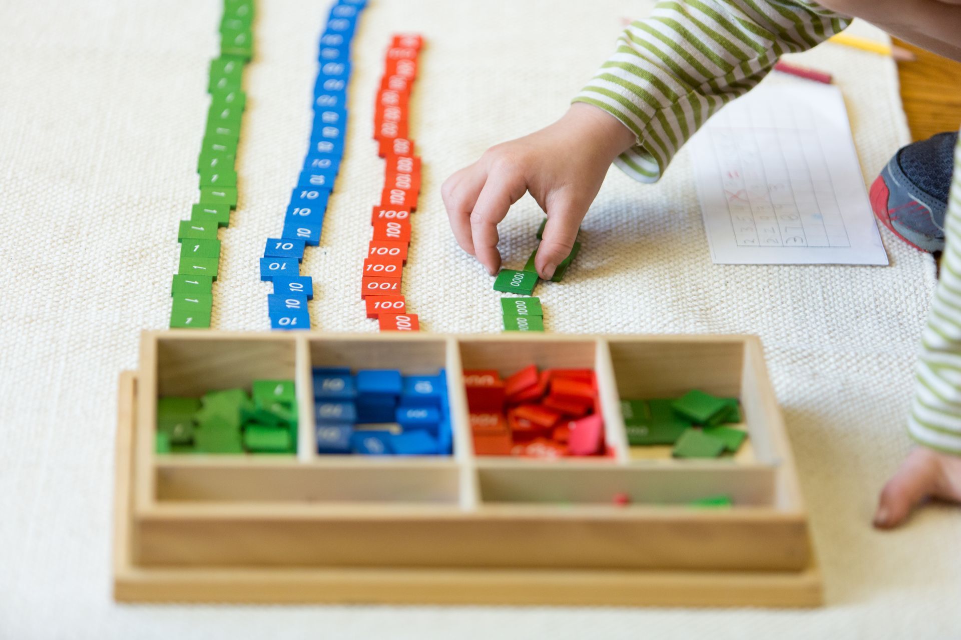 A Montessori child is working with a wooden tray filled with colorful blocks.