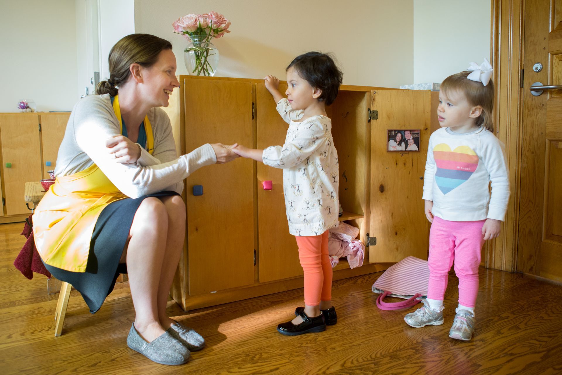 A guide is shaking hands with two Montessori children in a room.