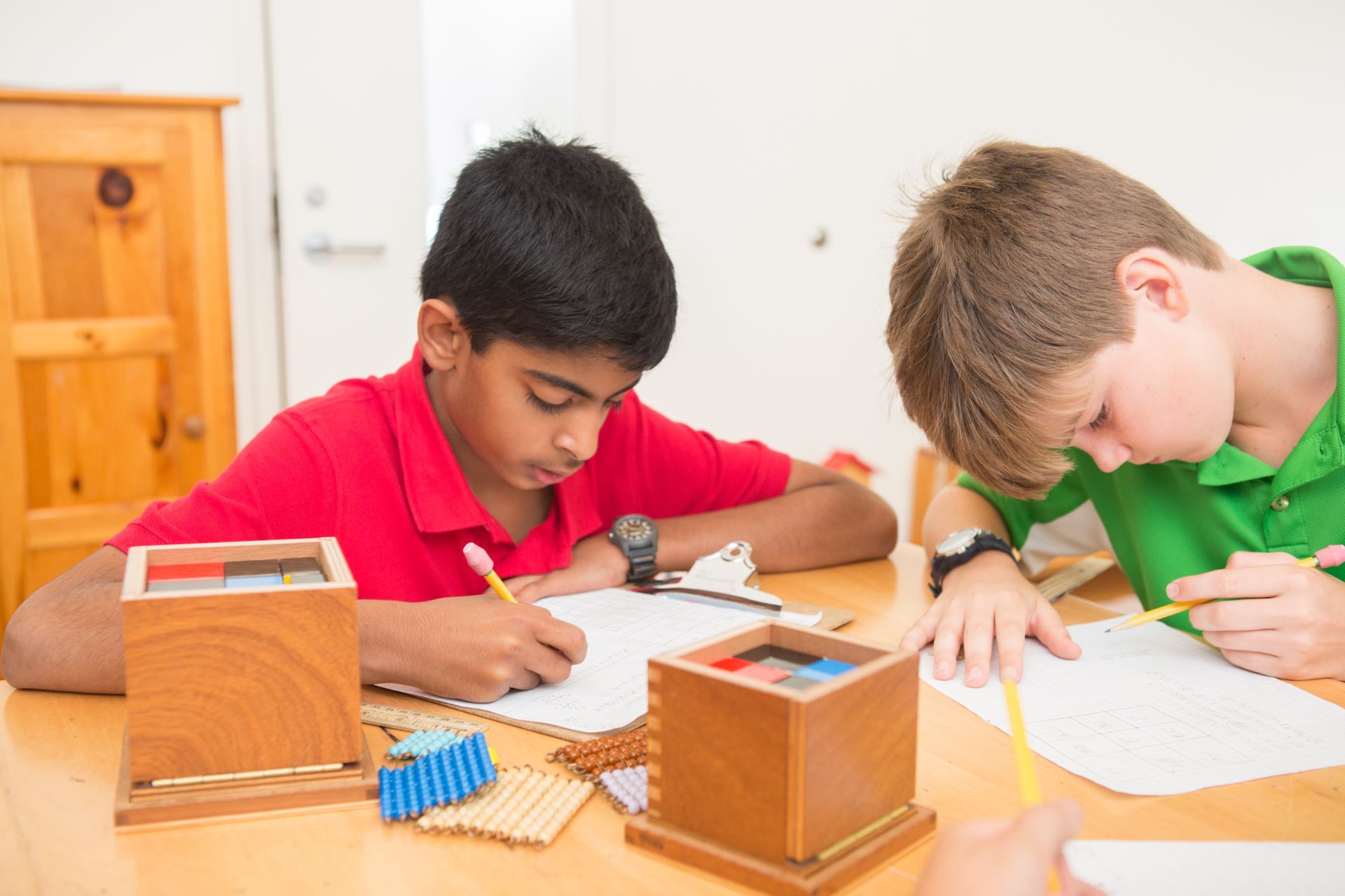 Montessori children are sitting at a table writing in a notebook.